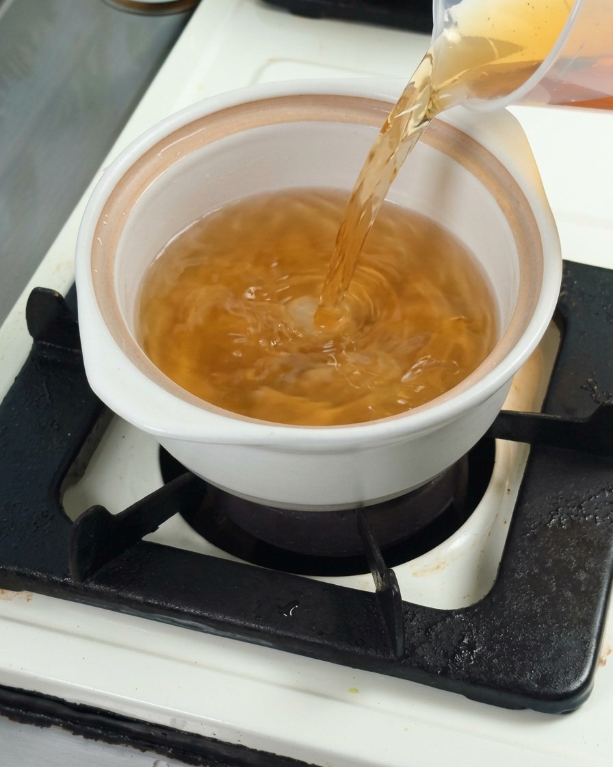 Bouillon de kombu dashi versé dans une casserole en céramique blanche pour préparer la base de cuisson.