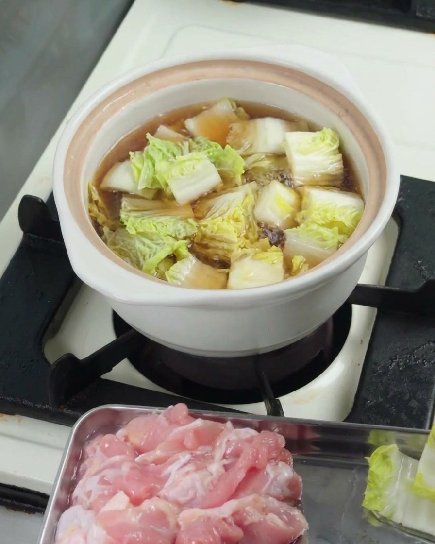 Bébé bok choy haché mijotant dans le bouillon à lintérieur dune casserole blanche couverte.