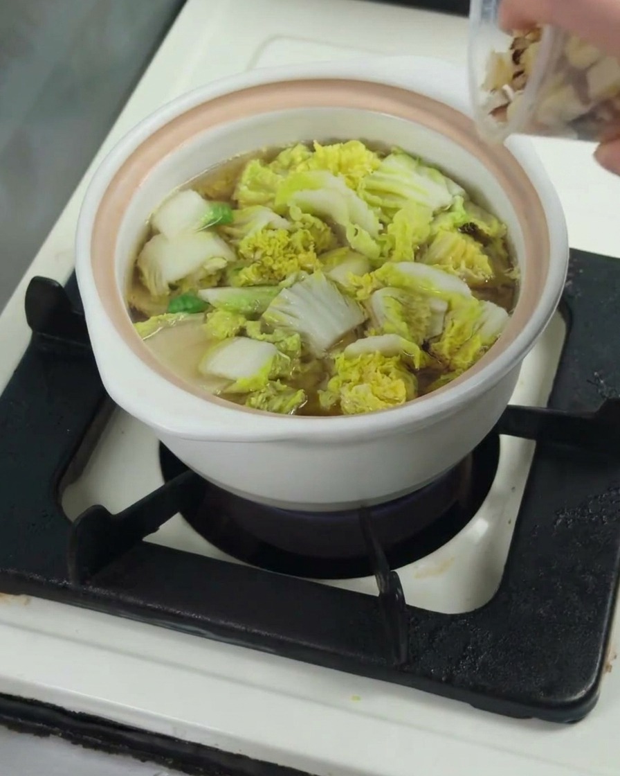 Morceaux de cuisse de poulet crus ajoutés dans la casserole avec le bok choy et le bouillon.