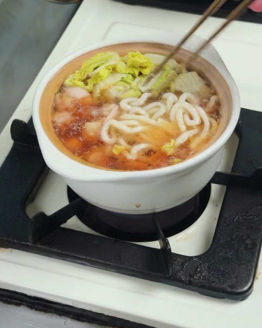 Nouilles udon ajoutées dans la casserole de bouillon, de poulet et de bok choy.