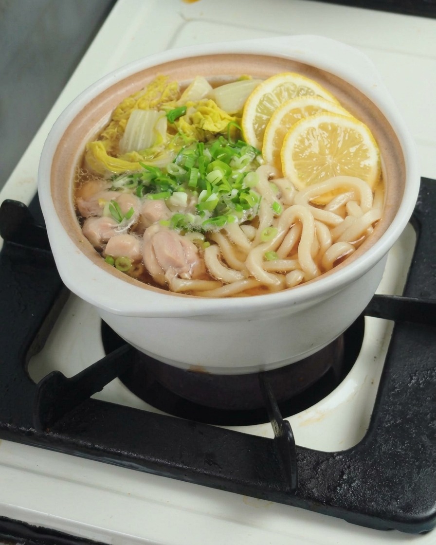 Main pressant un quartier de citron frais dans une casserole contenant des nouilles udon et du bok choy.