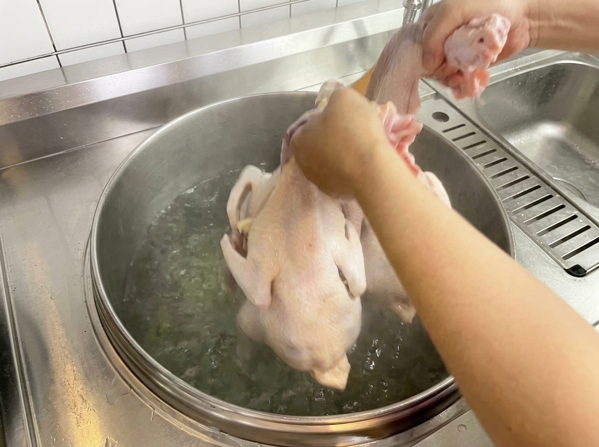 Un poulet cru plongé manuellement dans une grande casserole deau bouillante.