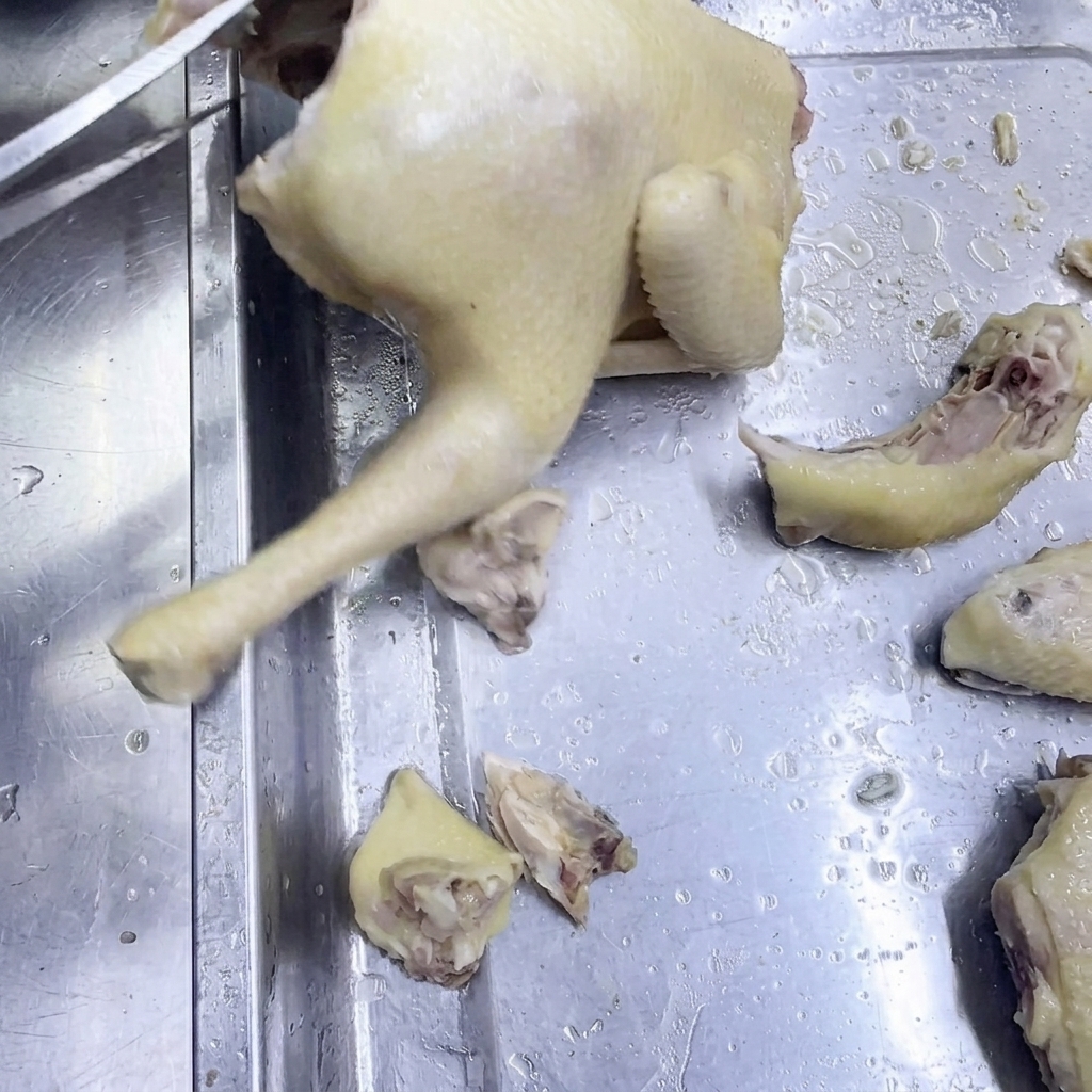 Utilisation de ciseaux de cuisine pour découper un poulet cuit sur une surface en inox.