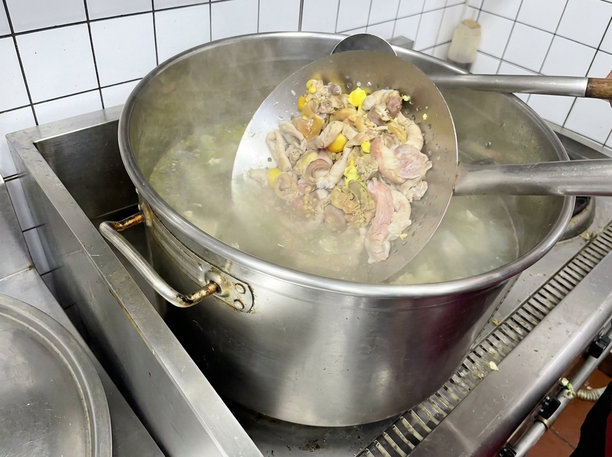 Abats de poulet blanchis dans une passoire métallique au-dessus deau bouillante.
