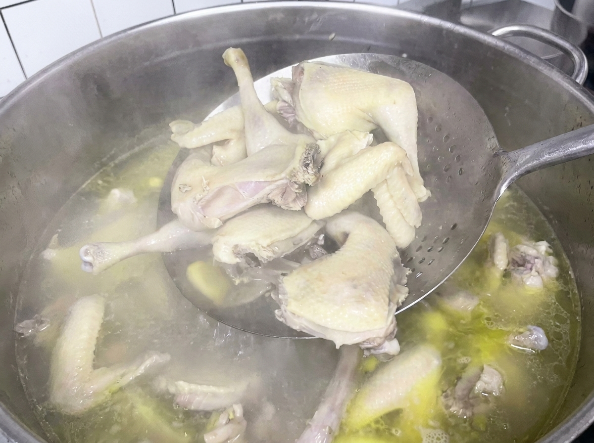 Morceaux de poulet retirés du bouillon avec une araignée de cuisine.