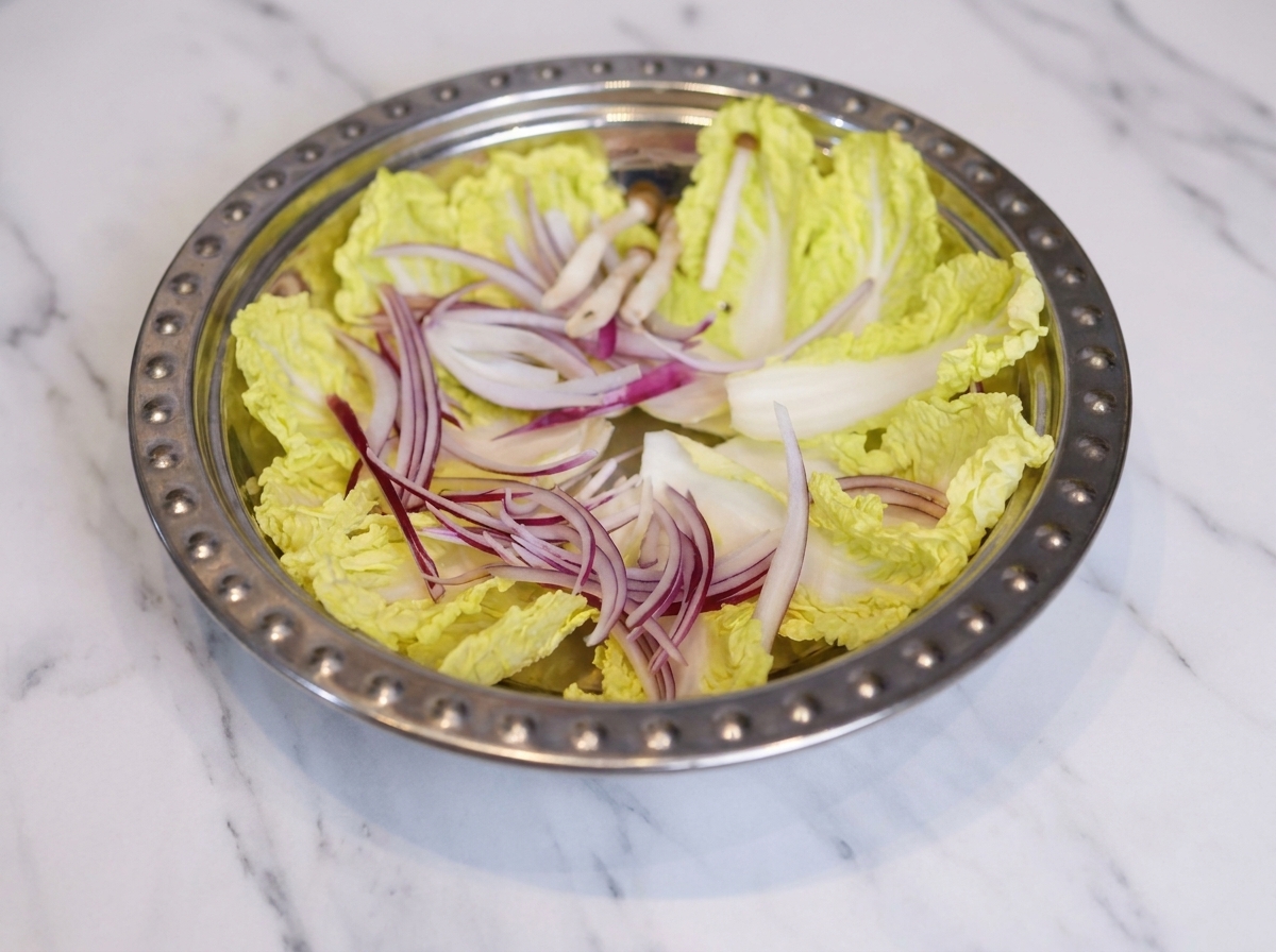 Une large marmite en métal remplie dun arrangement organisé de chou, doignons en lamelles, de champignons, de gâteaux de poisson et de tranches de luncheon meat.