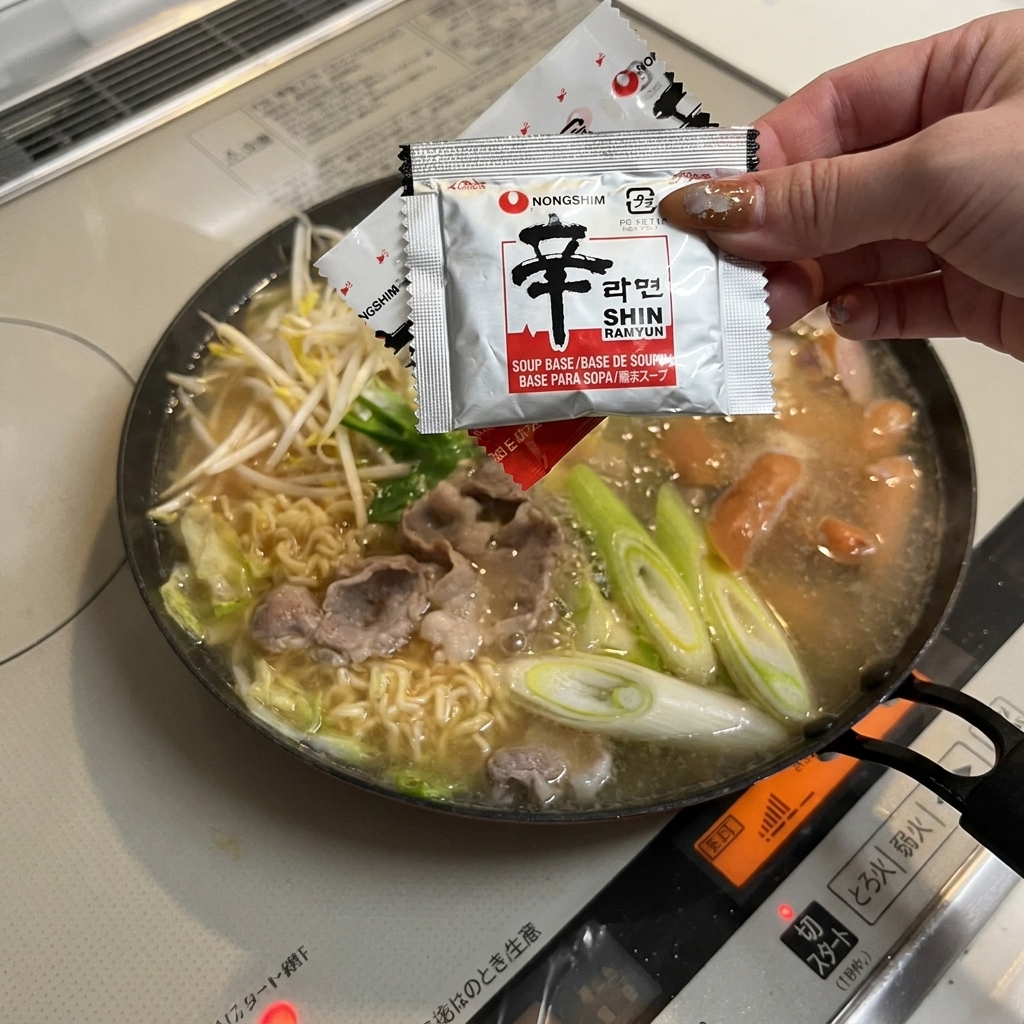Une main vidant le sachet dassaisonnement rouge pour nouilles instantanées dans la poêle mijotante.
