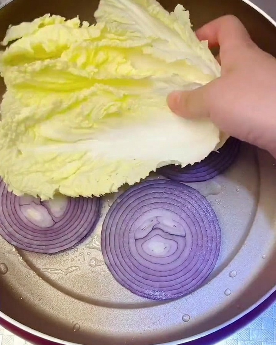 Feuilles de chou Napa frais placées dans la poêle sur les oignons sautés.
