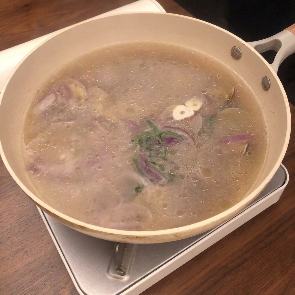 Le jus de cuisson des palourdes filtré à travers une passoire fine dans un bol en verre.