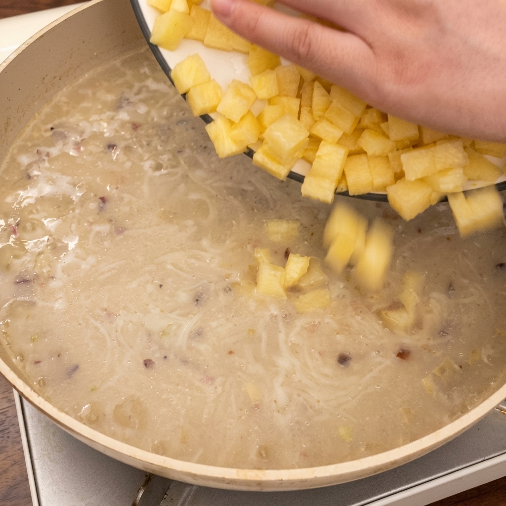 Une main déposant des cubes de pommes de terre dans la soupe frémissante.