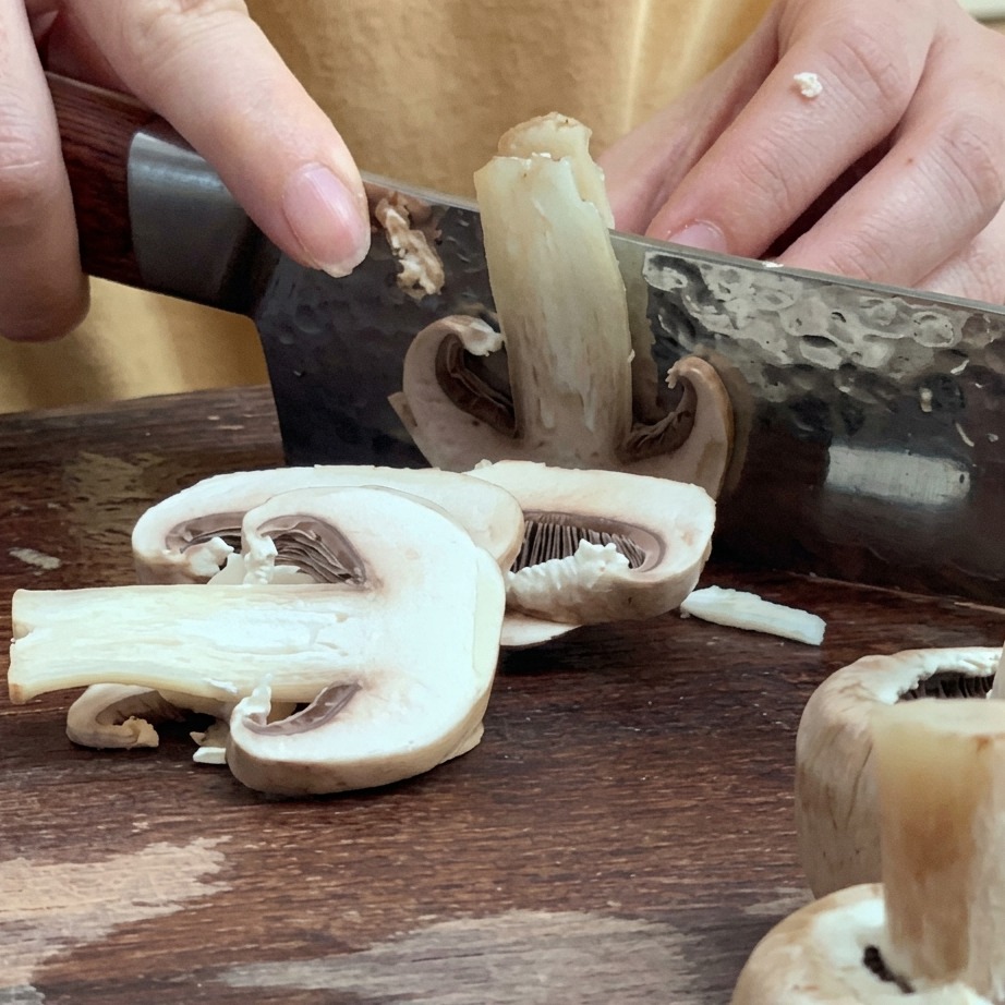 Champignons frais coupés en fines lamelles sur une planche à découper en bois.