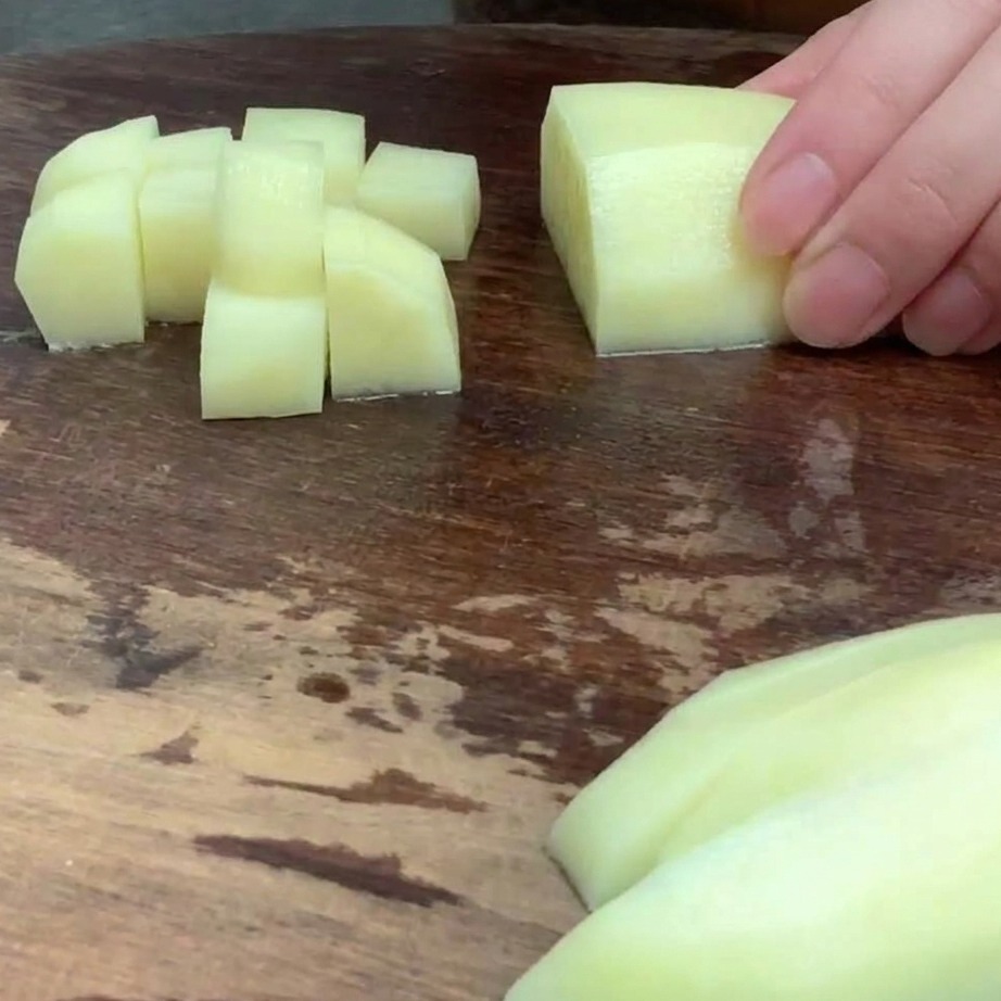 Pomme de terre épluchée coupée en petits dés réguliers sur une planche à découper.