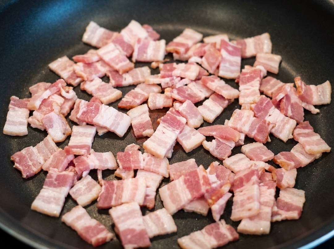 Morceaux de lard frits dans une poêle, libérant leur gras parfumé.