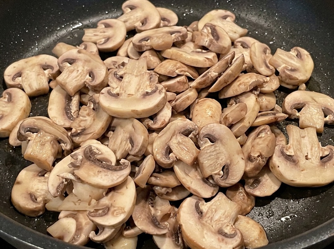 Champignons tranchés cuisant dans la poêle avec les morceaux de lard.