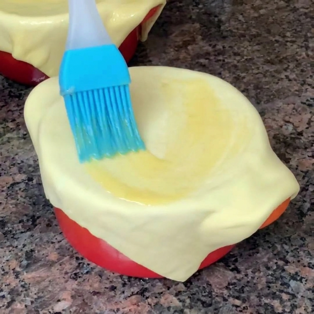 Gros plan dun pinceau en silicone bleu étalant de lœuf battu sur la pâte feuilletée recouvrant un bol.