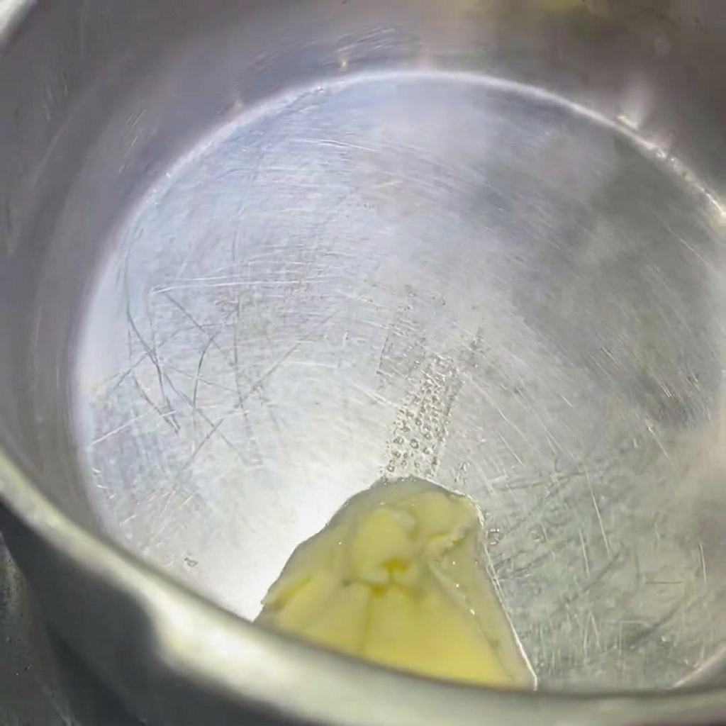 Gros plan sur une noisette de beurre fondant dans une casserole en acier inoxydable.