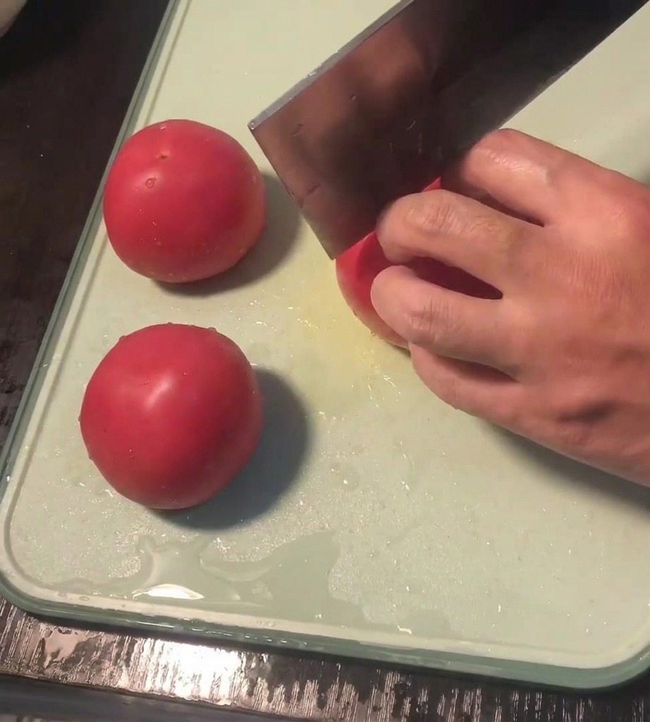 Vue rapprochée dune main utilisant un couteau pour inciser une croix sur la peau dune tomate fraîche sur une planche à découper.