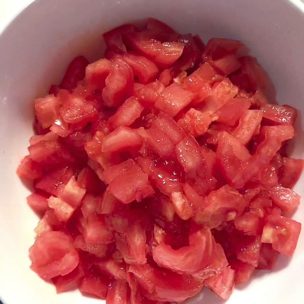 Un bol blanc rempli de tomates fraîchement coupées en dés et pelées.