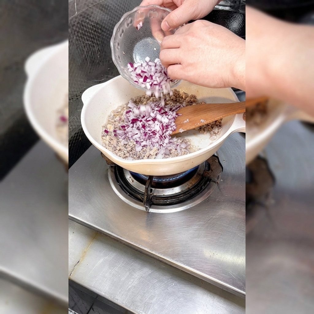 Oignons en dés ajoutés dans une poêle remplie de viande hachée dorée.