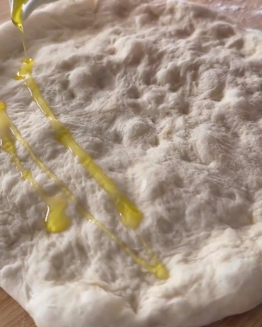 Huile dolive versée sur la pâte à pizza crue, étirée et parsemée de creux.