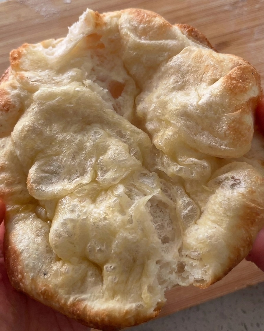 Pain pizza fraîchement cuit et boursouflé, ouvert délicatement avec les mains.