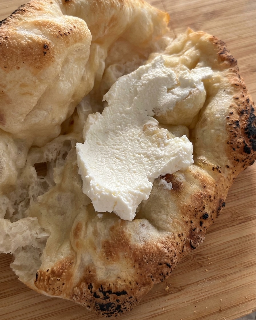 Couche épaisse de ricotta blanche étalée à lintérieur dun pain pizza fraîchement cuit et ouvert.