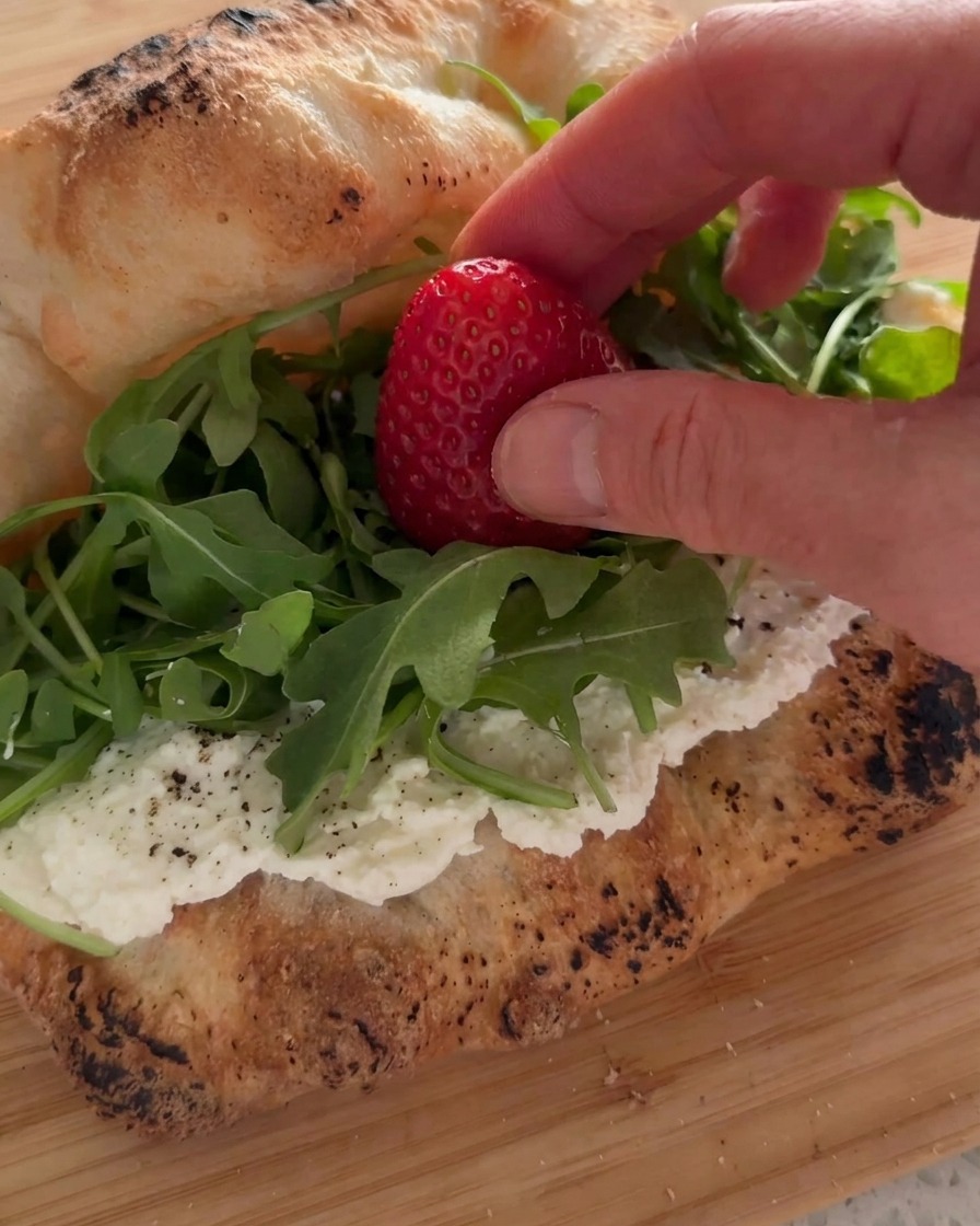 Main déposant une fraise fraîche sur un lit de roquette verte à lintérieur du sandwich à la ricotta.