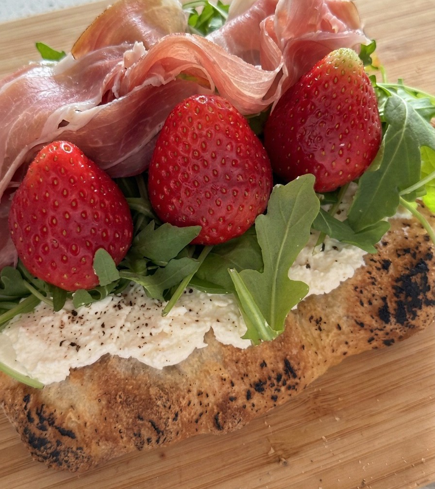 Gros plan sur des tranches de prosciutto pliées et déposées sur les fraises et la roquette.
