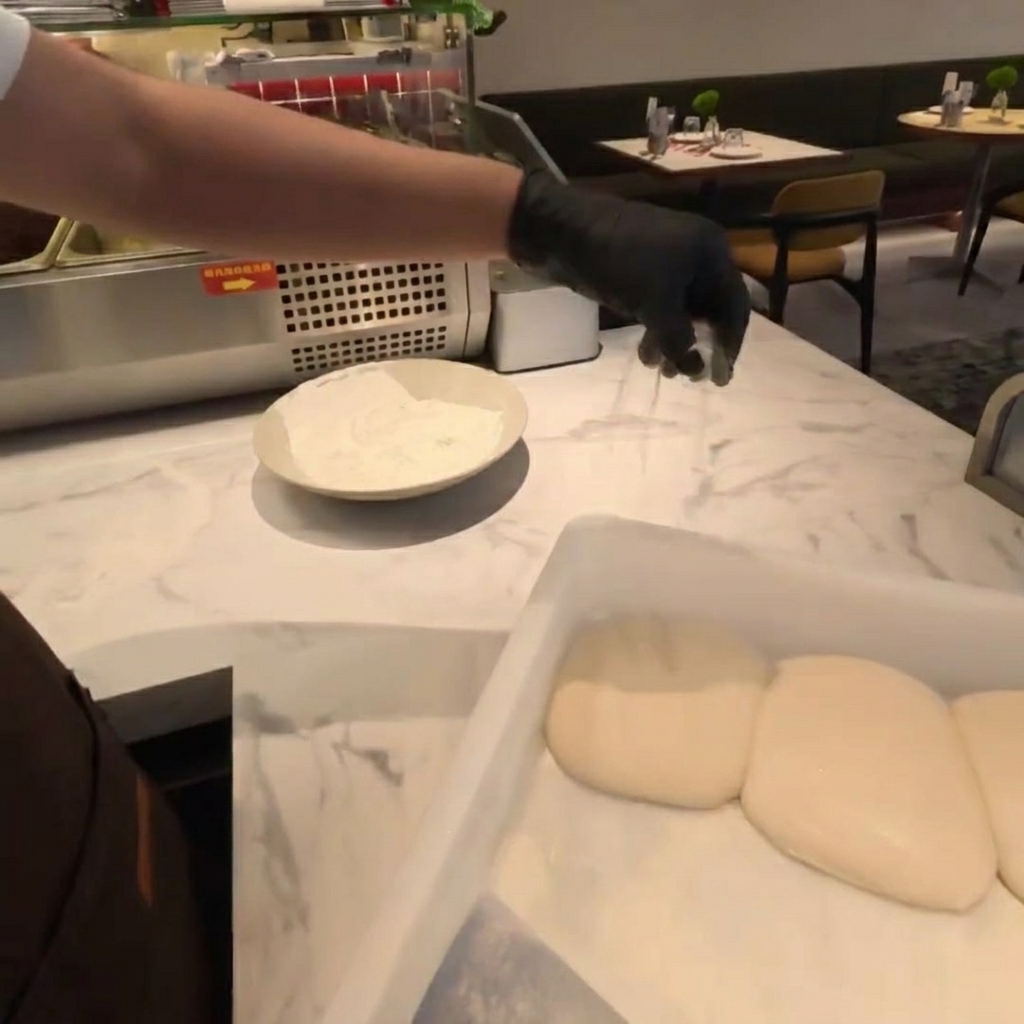 Farine saupoudrée sur des pâtons de pizza sur un comptoir en marbre.