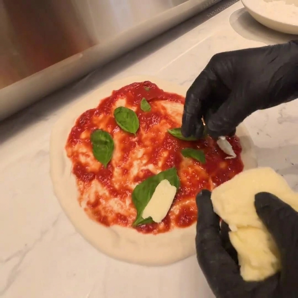 Morceaux de mozzarella fraîche disposés sur une couche de roquette sur la pâte crue.