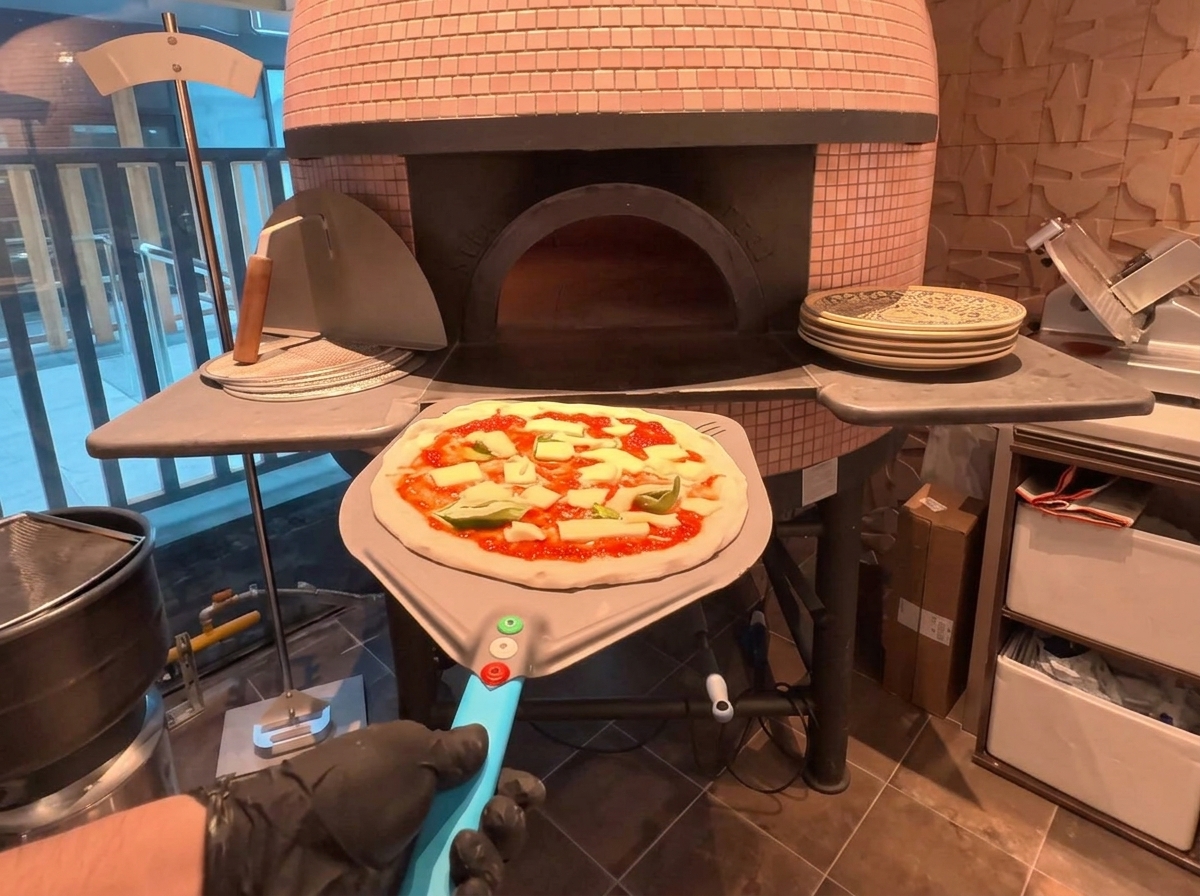 Une pizza sur une pelle métallique étant glissée dans un four à bois traditionnel.