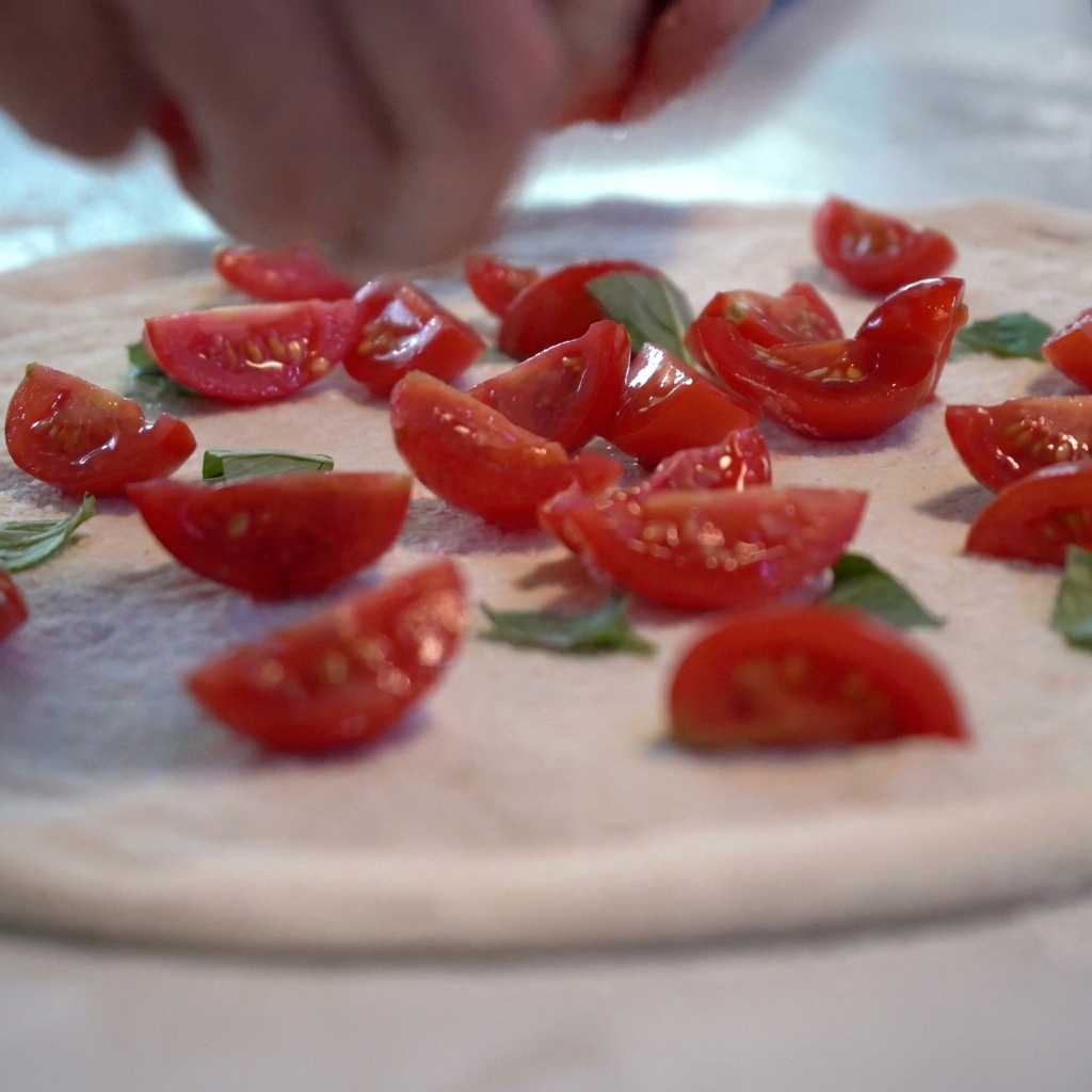 Sauce tomate et tranches de tomates fraîches ajoutées sur la base de pâte à pizza crue.