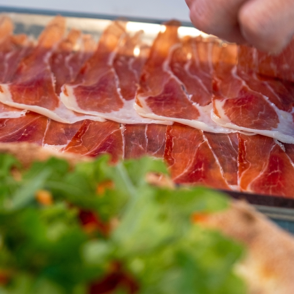 De fines tranches de prosciutto soigneusement disposées sur la pizza garnie de roquette.