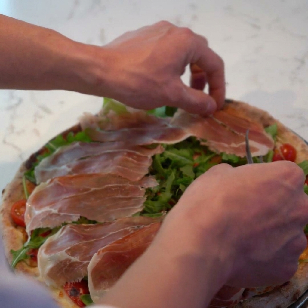 Parmesan râpé saupoudré sur la pizza, recouvrant le prosciutto et la roquette.