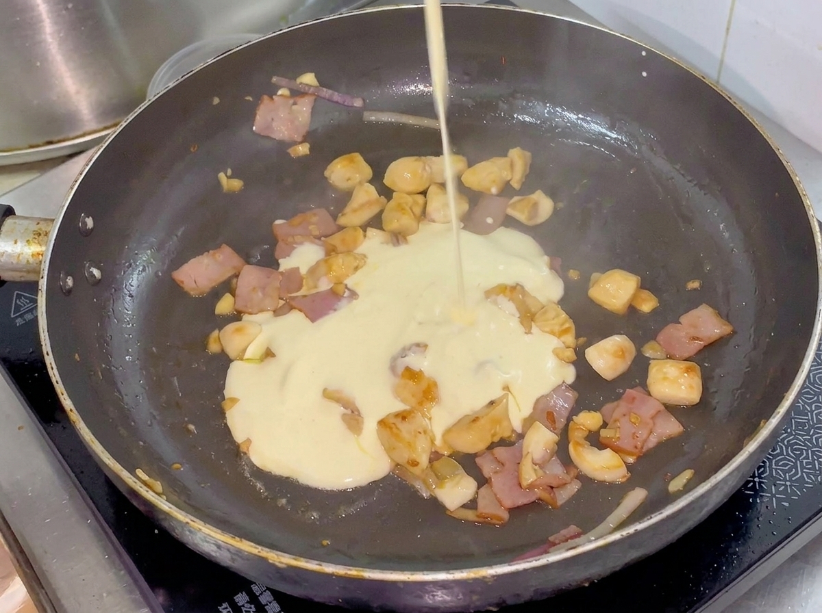 De la crème versée dun petit pichet dans une poêle contenant le poulet, le bacon et les légumes cuits.