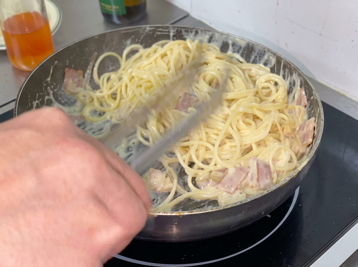 Une portion de spaghettis cuits ajoutée dans une sauce crémeuse dans une poêle.