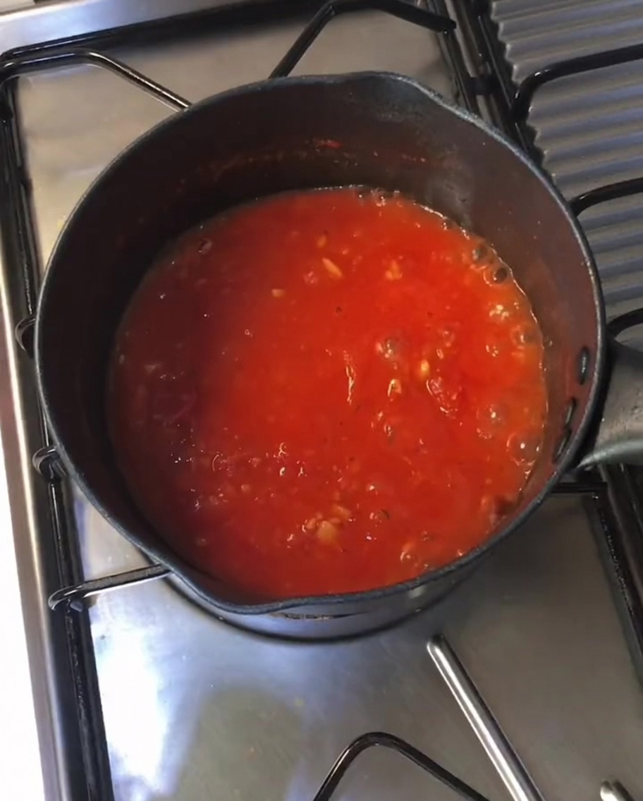 Une sauce tomate rouge, épaisse et frémissante dans une poêle noire sur la cuisinière.