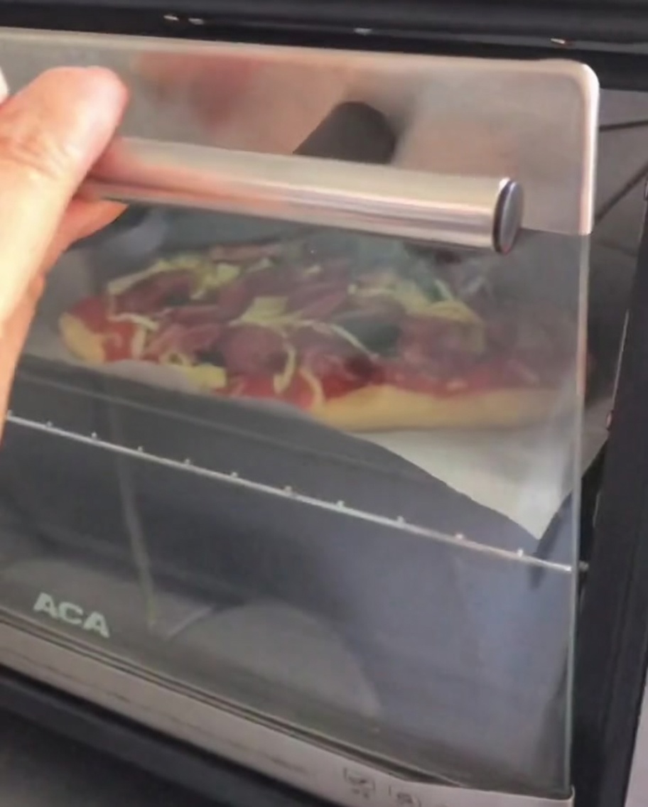 Ouverture de la porte dun petit four de comptoir pour y placer une pizza crue et garnie sur une plaque de cuisson.