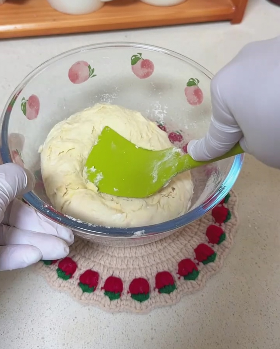 Mains gantées utilisant une spatule en silicone pour mélanger la pâte dans un bol.