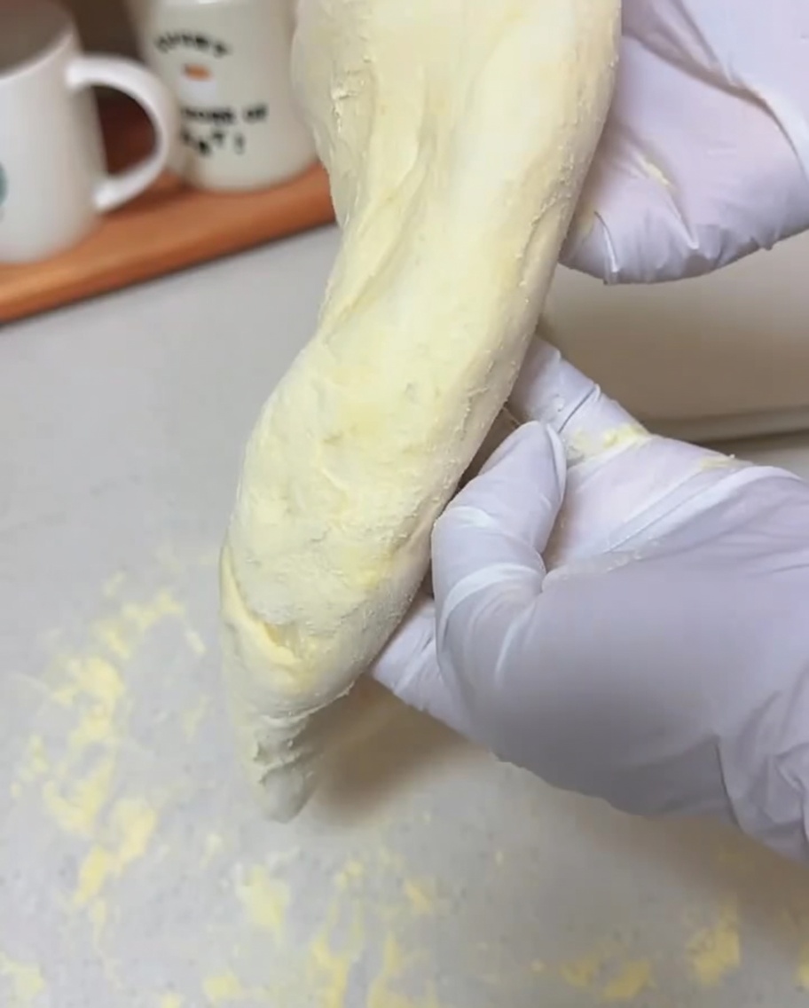 Mains gantées tenant une portion de pâte, la laissant sétirer par gravité.