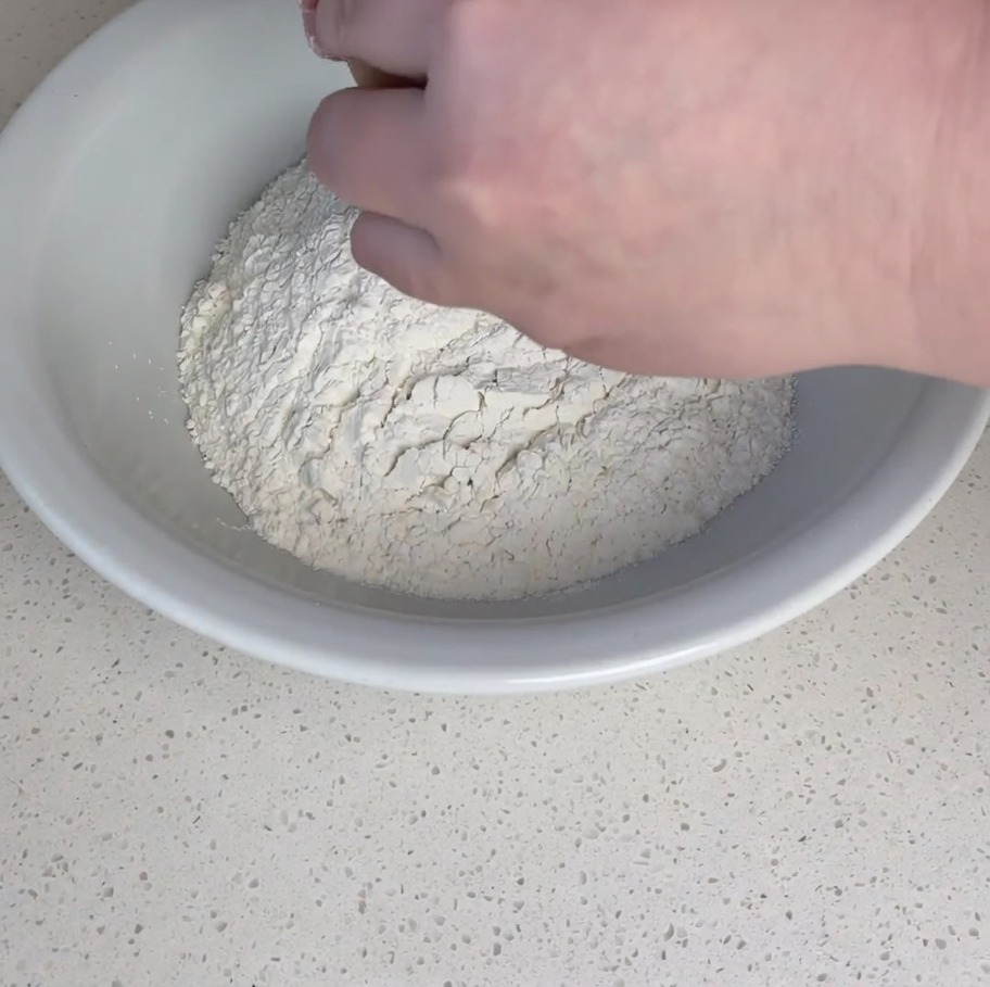 Mains cassant un œuf cru dans un puits de farine riche en gluten.