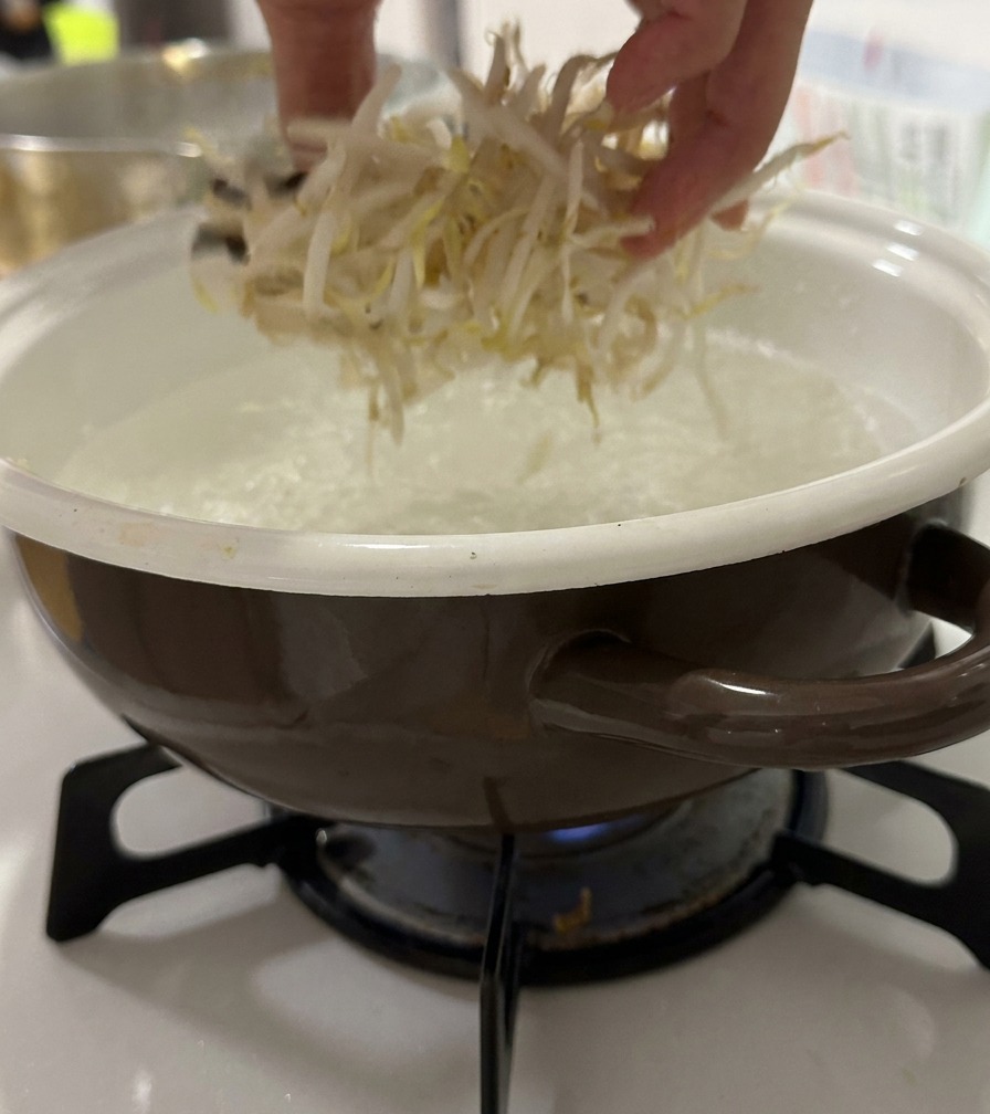 Une main jetant des pousses de soja fraîches dans une casserole deau bouillante.