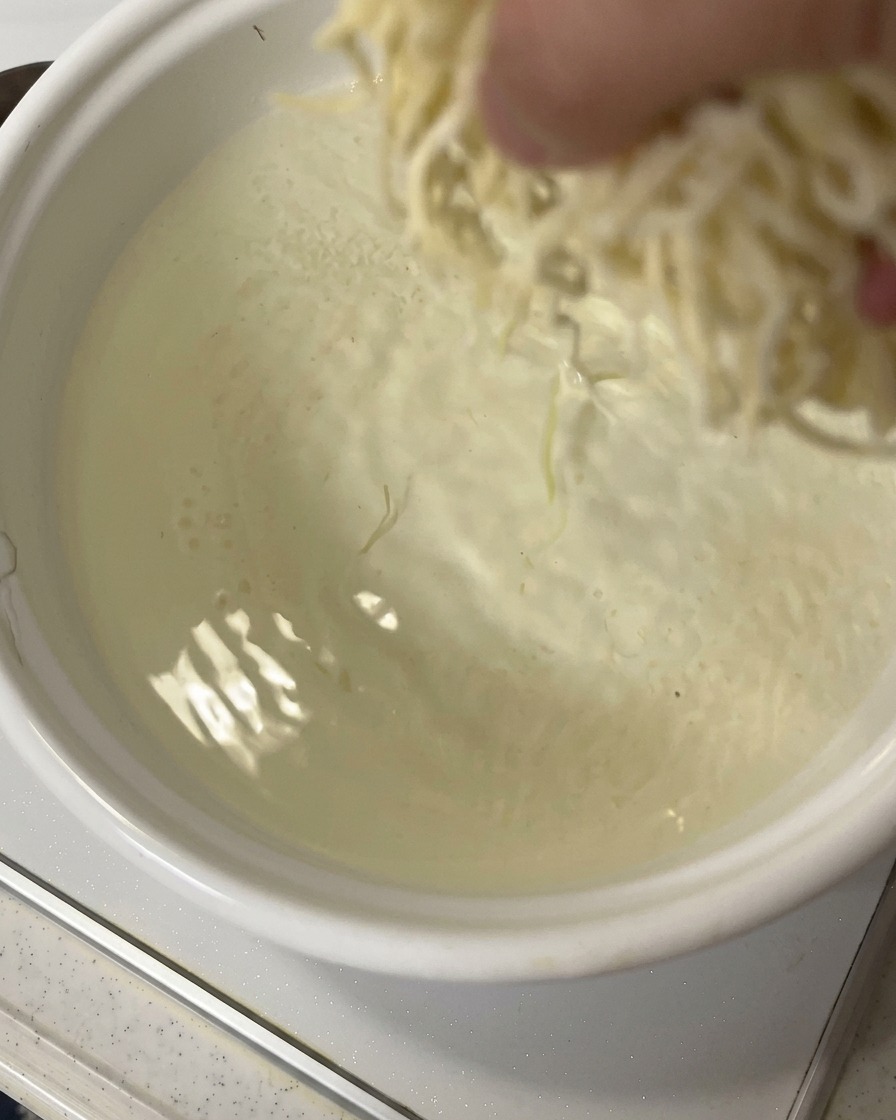 Une main jetant une portion de nouilles ramen fraîches dans une casserole deau en ébullition rapide.