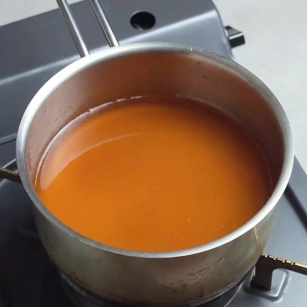 Une casserole contenant une base de soupe ramen ambrée sombre mijotant sur feu moyen.