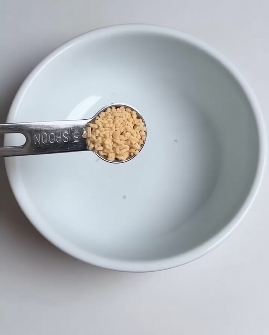 Gros plan dune cuillère à mesurer versant du bouillon de poulet en poudre dans un bol blanc.