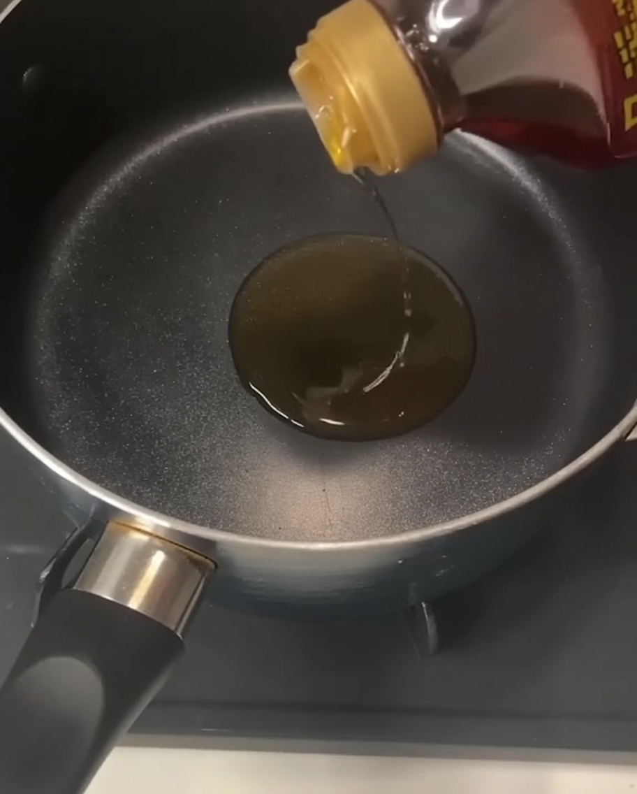 Une bouteille versant de lhuile de sésame dorée dans une casserole noire vide sur une plaque de cuisson.