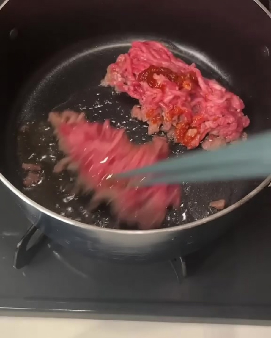 Baguettes soulevant et mélangeant des morceaux de porc haché enrobés de pâte pimentée rouge dans une casserole.