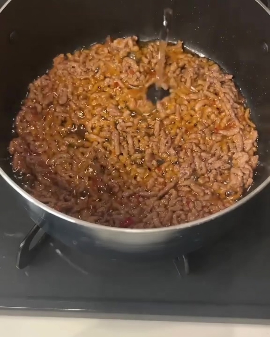 Liquide clair versé dans une casserole contenant du porc haché cuit et assaisonné.
