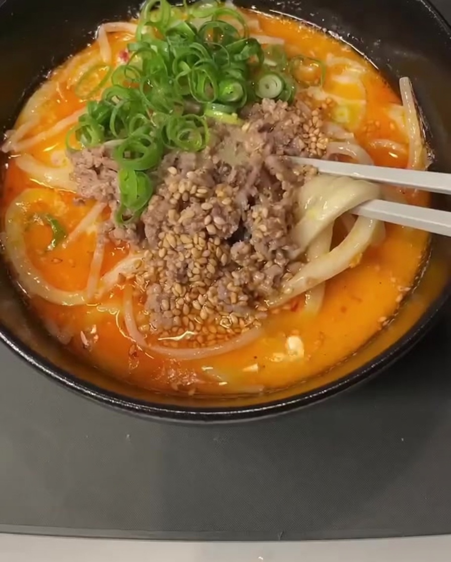 Vue rapprochée dune casserole contenant un mélange liquide crémeux avec une cuillère de pâte miso en cours dincorporation.