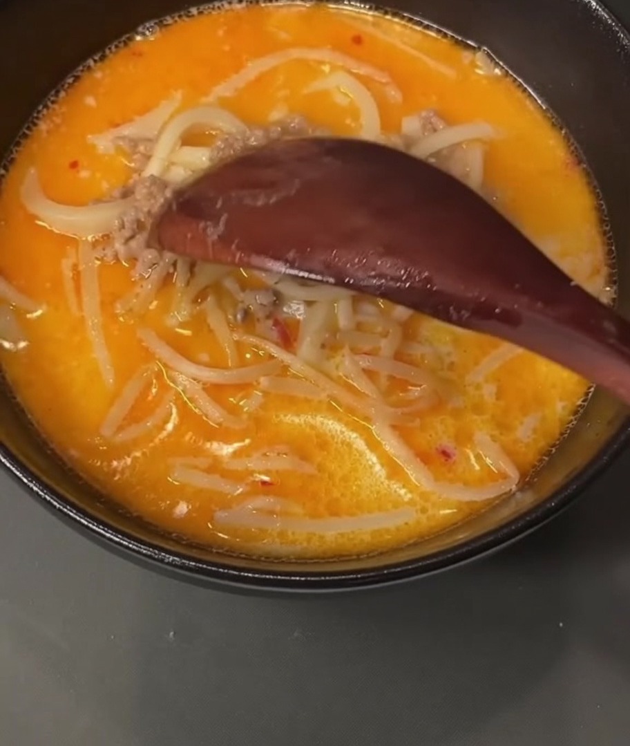 Une cuillère en bois ramassant du porc haché cuit dans une casserole remplie de bouillon.